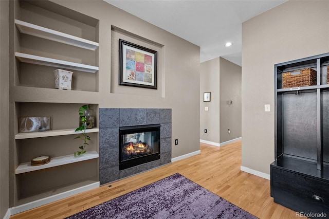 living room featuring hardwood / wood-style floors, built in features, and a tile fireplace