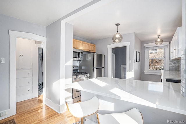 kitchen with hanging light fixtures, stainless steel appliances, light hardwood / wood-style floors, kitchen peninsula, and light brown cabinets