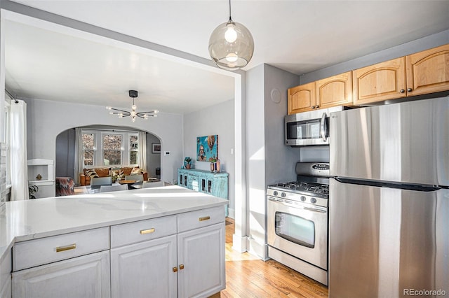 kitchen with light brown cabinetry, decorative light fixtures, ceiling fan, stainless steel appliances, and light hardwood / wood-style floors