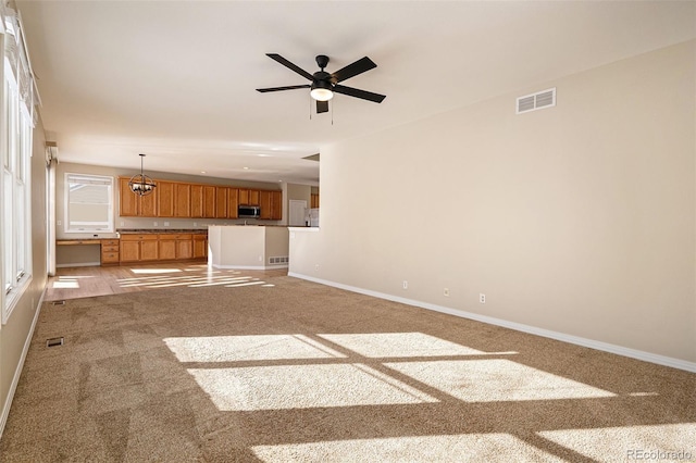 unfurnished living room with carpet and ceiling fan with notable chandelier