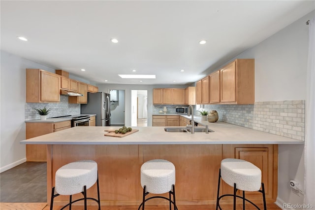 kitchen with under cabinet range hood, a peninsula, a kitchen breakfast bar, light countertops, and appliances with stainless steel finishes