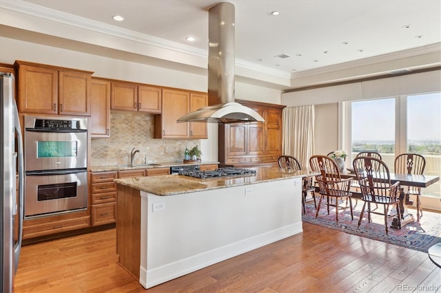 kitchen with light stone countertops, a sink, island exhaust hood, crown molding, and appliances with stainless steel finishes