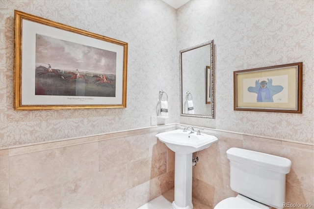 bathroom featuring toilet, tile walls, wainscoting, and wallpapered walls