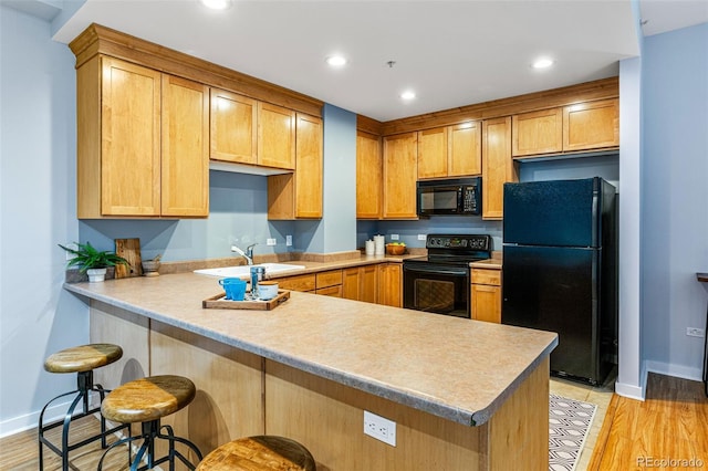 kitchen featuring sink, light hardwood / wood-style flooring, a breakfast bar, black appliances, and kitchen peninsula