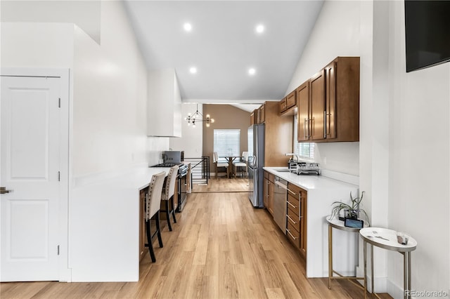 kitchen featuring a kitchen bar, appliances with stainless steel finishes, light hardwood / wood-style flooring, a chandelier, and lofted ceiling