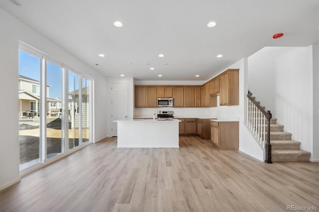 kitchen with an island with sink, stainless steel appliances, and light wood-type flooring