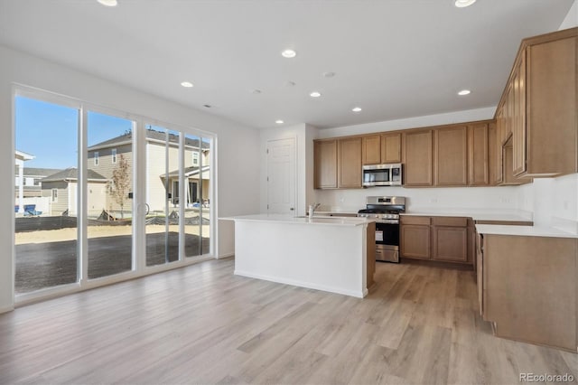 kitchen featuring stainless steel appliances, light hardwood / wood-style flooring, and a center island with sink