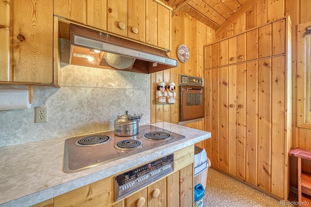 kitchen featuring lofted ceiling, stainless steel stovetop, black oven, and wooden walls