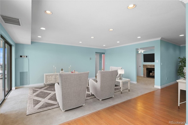 living room featuring ceiling fan, a tiled fireplace, crown molding, and light hardwood / wood-style flooring