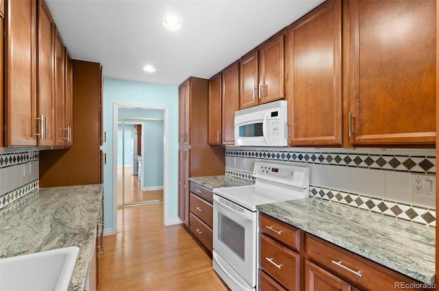 kitchen with backsplash, white appliances, light stone countertops, and light hardwood / wood-style floors