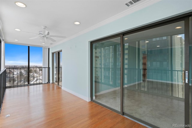 unfurnished room with ornamental molding, expansive windows, ceiling fan, and wood-type flooring