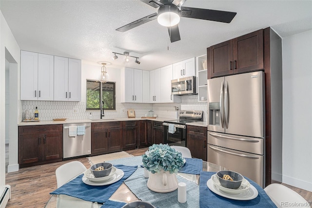 kitchen featuring a baseboard radiator, stainless steel appliances, a sink, light countertops, and light wood finished floors