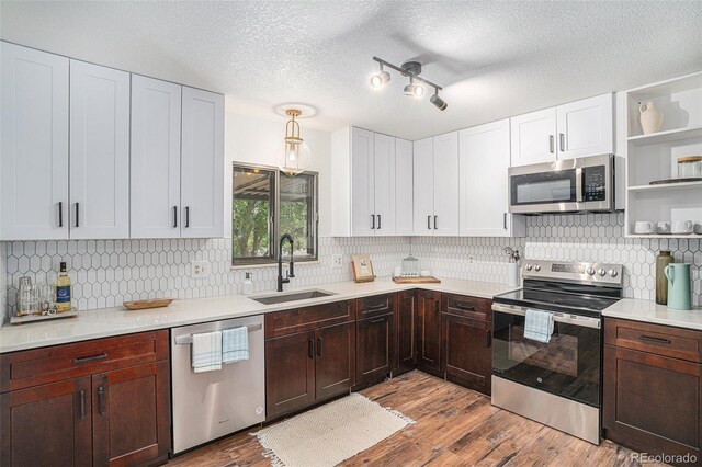 kitchen featuring pendant lighting, open shelves, stainless steel appliances, light countertops, and a sink