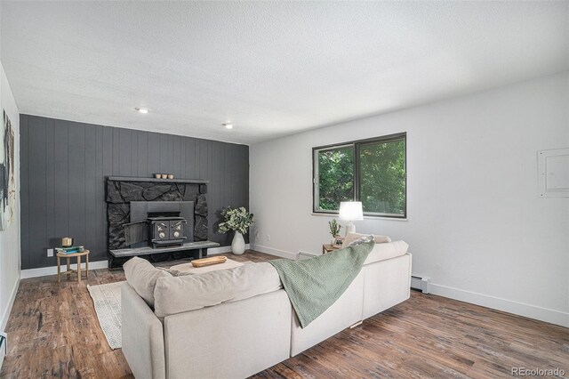 living area featuring baseboards, wood finished floors, a wood stove, baseboard heating, and a textured ceiling