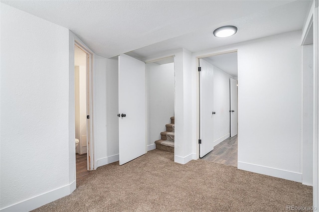 below grade area featuring light carpet, a textured ceiling, baseboards, and stairs