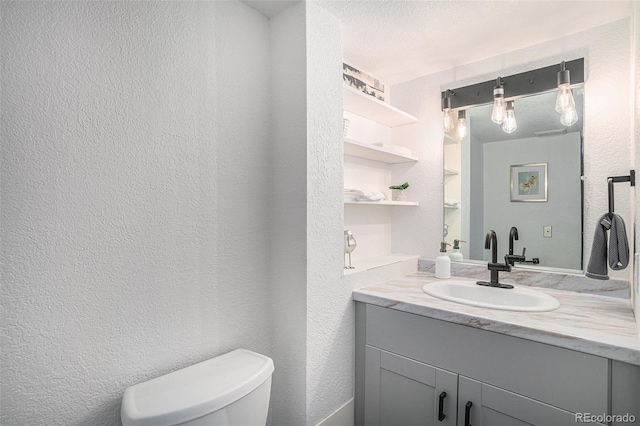 bathroom with toilet, a textured wall, and vanity