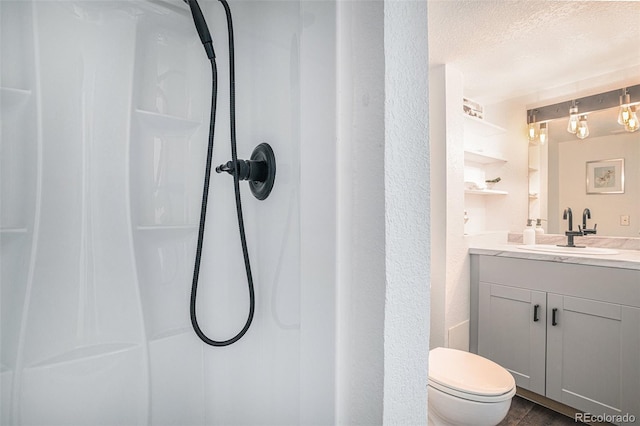 bathroom featuring toilet, vanity, a textured ceiling, and walk in shower