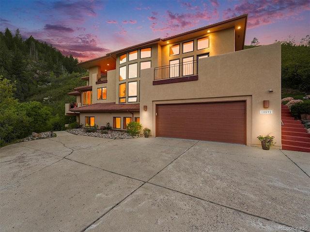 view of front of house with an attached garage, stucco siding, driveway, and a balcony