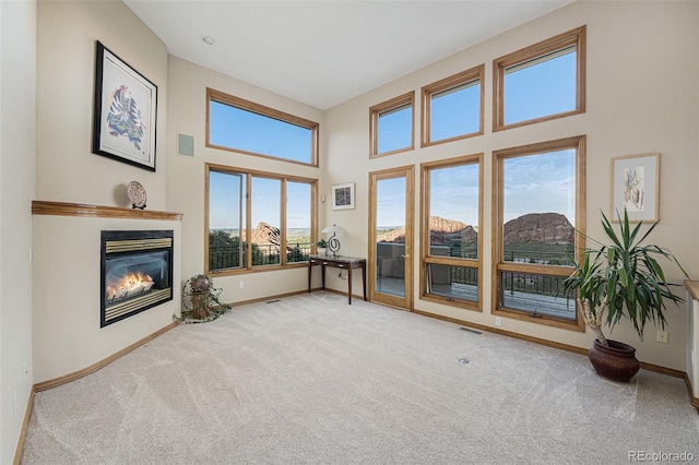 carpeted living room featuring baseboards, a towering ceiling, and a glass covered fireplace