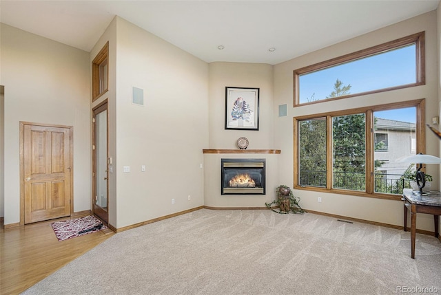 living area with baseboards, a glass covered fireplace, visible vents, and a high ceiling