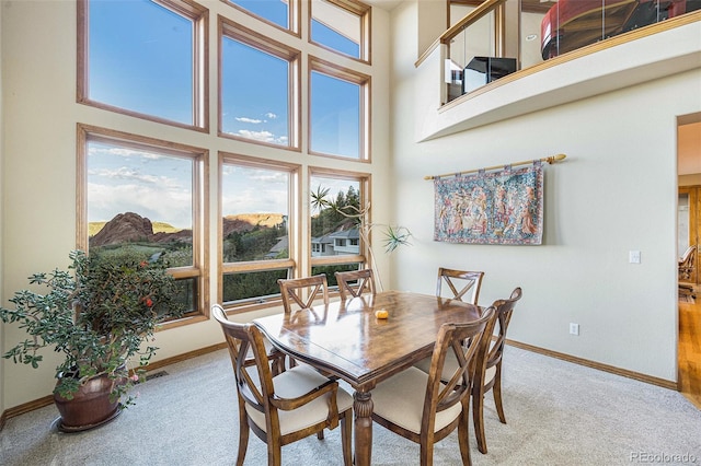 dining room featuring light colored carpet, a high ceiling, and baseboards