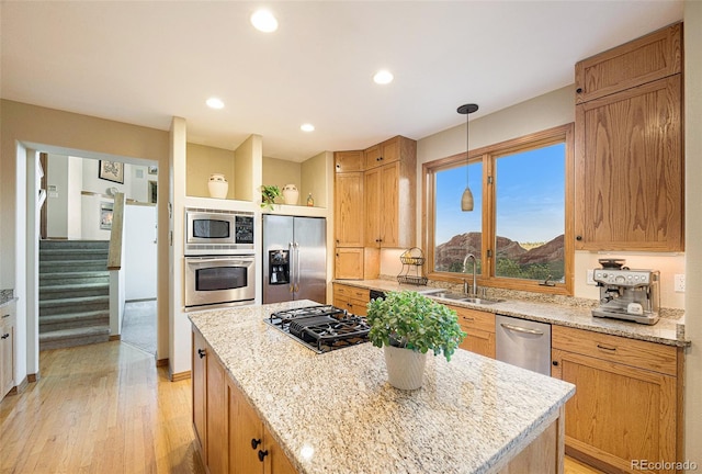 kitchen featuring a sink, stainless steel appliances, light wood-type flooring, a center island, and light stone countertops