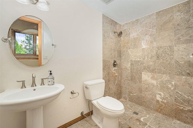 full bath featuring a sink, toilet, baseboards, and a tile shower