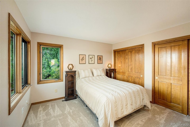bedroom with baseboards, light carpet, and multiple closets