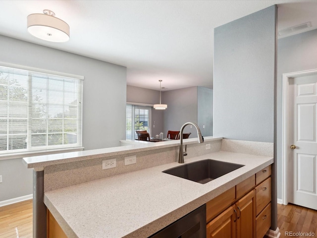 kitchen featuring light stone counters, decorative light fixtures, sink, and light hardwood / wood-style floors