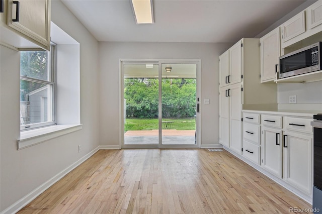 2709 S Franklin St, Denver, CO 80210 - kitchen with stainless steel microwave, light wood-type flooring, white cabinetry, and light countertops