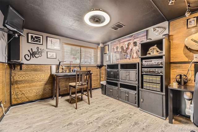 home office with visible vents, a textured ceiling, wood finished floors, and wooden walls