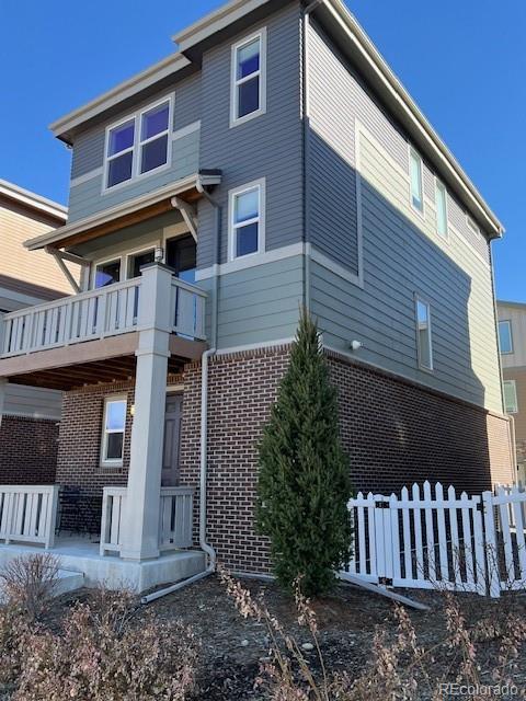 rear view of property with a balcony, fence, and brick siding