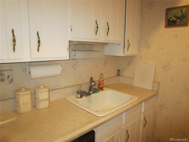 kitchen with white cabinetry, sink, and tile walls