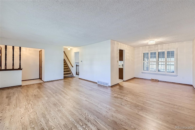 unfurnished living room with wood finished floors, visible vents, a textured ceiling, and stairs