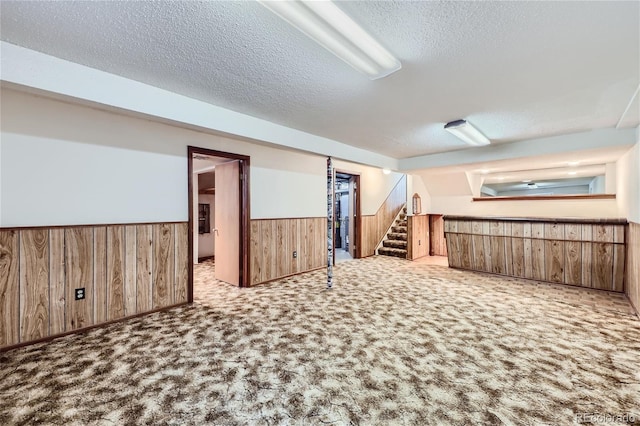 finished basement with a wainscoted wall, stairway, carpet flooring, wooden walls, and a textured ceiling