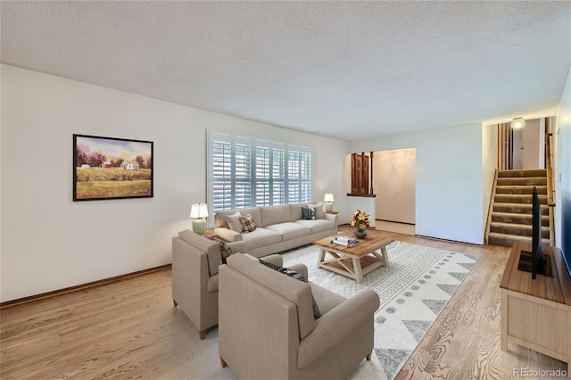 living room featuring light wood finished floors, stairs, baseboards, and a textured ceiling