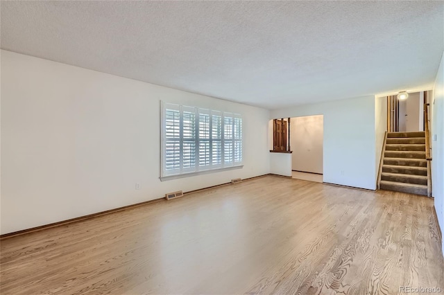 spare room with light wood-style floors, visible vents, stairway, and a textured ceiling