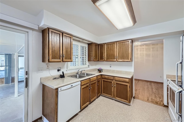 kitchen featuring brown cabinetry, white appliances, light countertops, and a sink