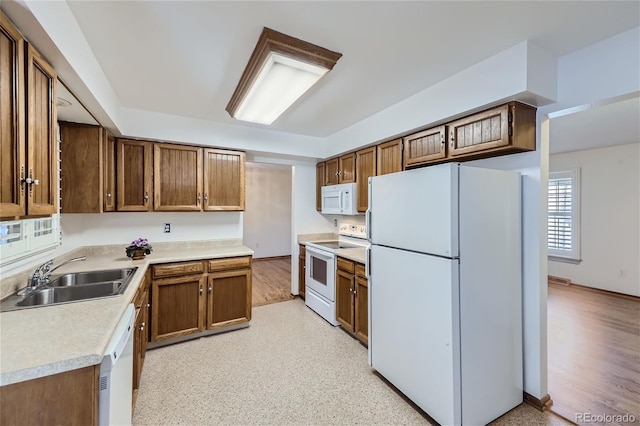 kitchen featuring light countertops, white appliances, brown cabinetry, and a sink