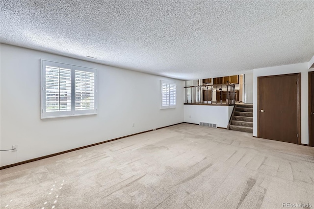 unfurnished living room with light carpet, baseboards, stairs, and visible vents