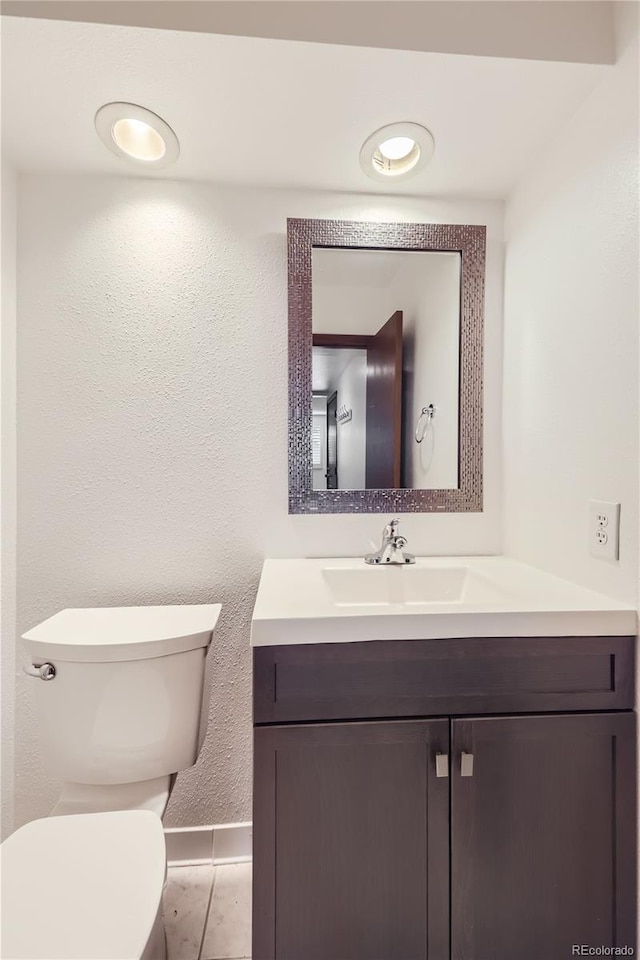 bathroom featuring toilet, a textured wall, and vanity