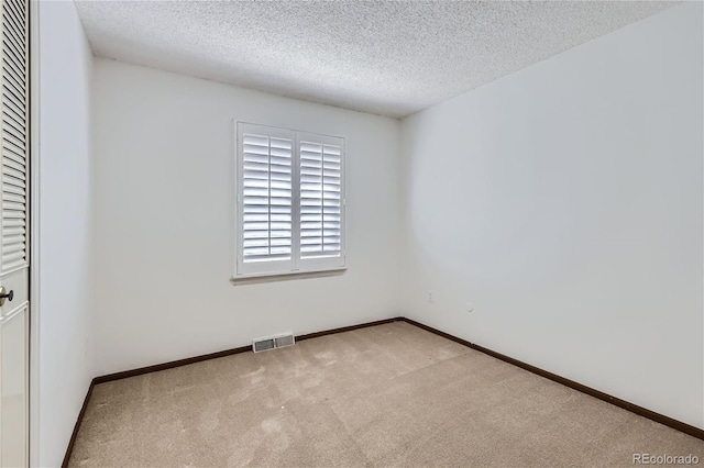 carpeted empty room featuring baseboards, visible vents, and a textured ceiling