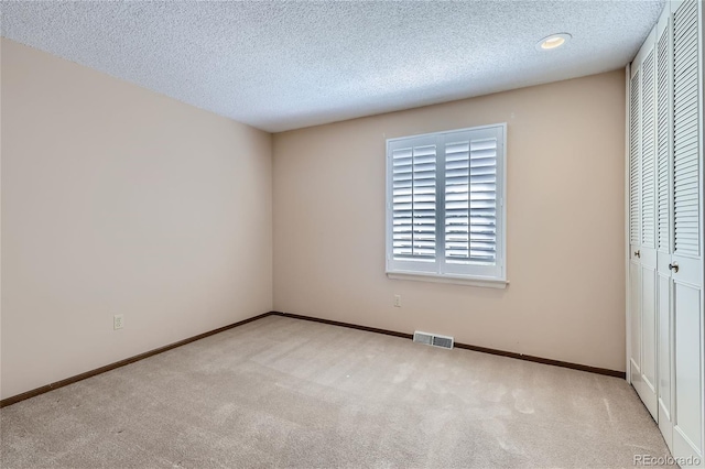 unfurnished bedroom featuring a textured ceiling, carpet floors, a closet, and visible vents