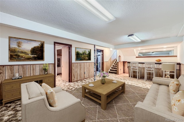 living area featuring stairs, wooden walls, a textured ceiling, and wainscoting