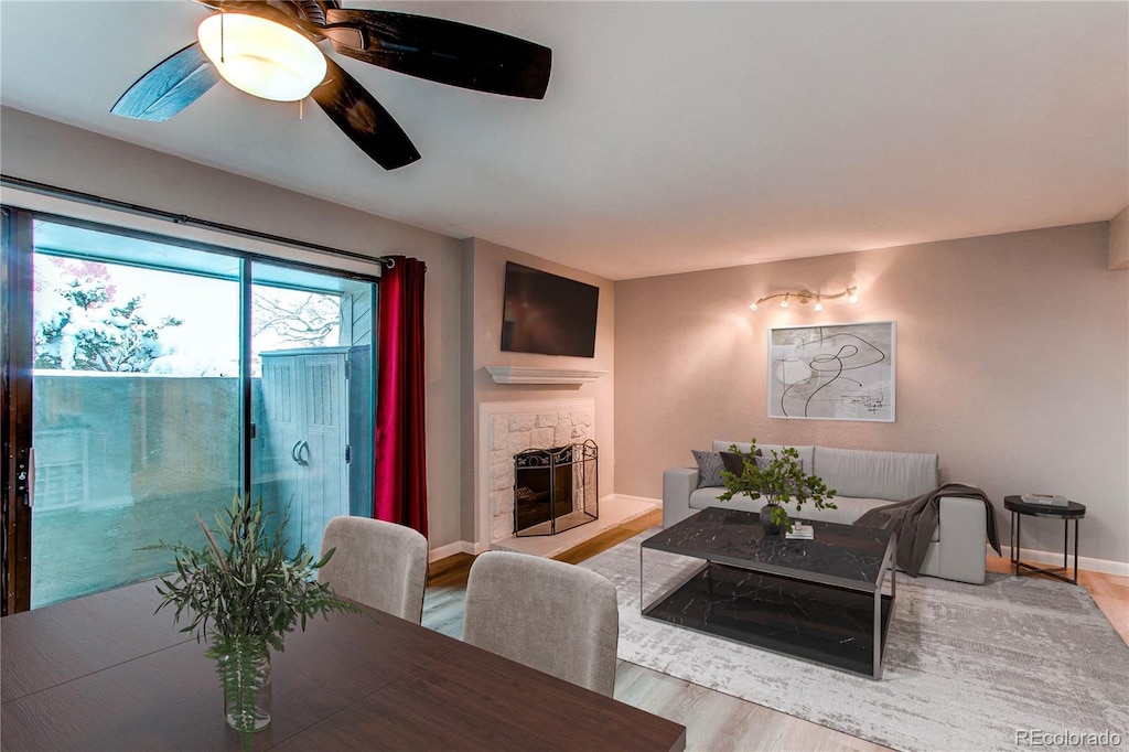 dining space with baseboards, a stone fireplace, a ceiling fan, and light wood-style floors