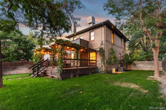 back house at dusk with a deck, a lawn, and central air condition unit