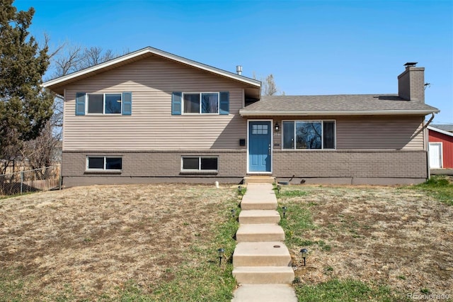 tri-level home with brick siding, fence, and a chimney