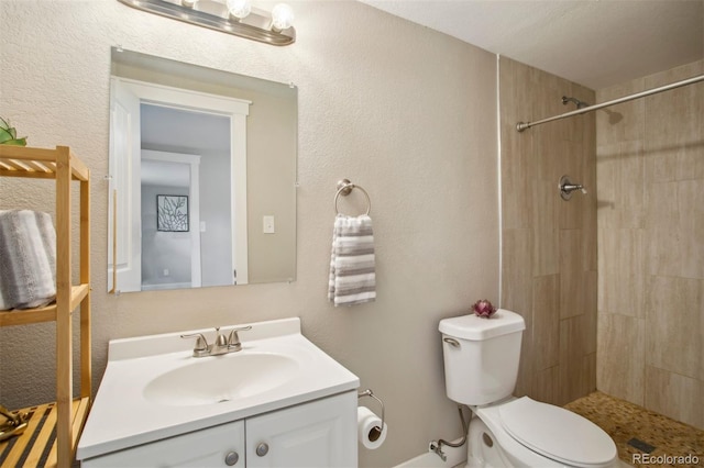 bathroom with a textured wall, a tile shower, toilet, and vanity