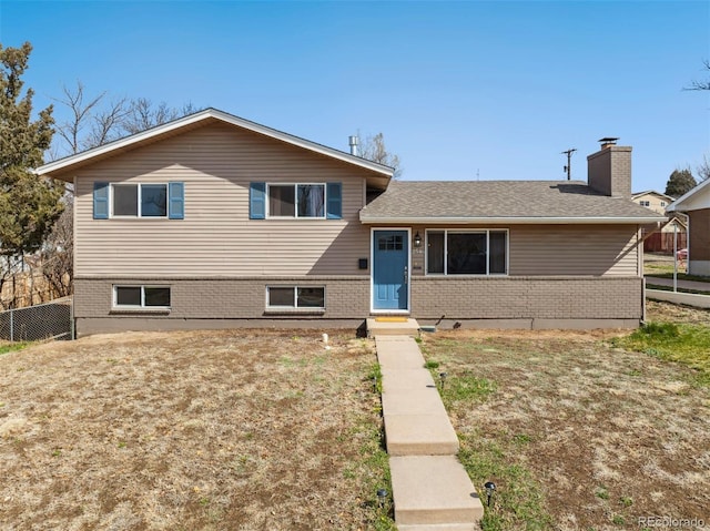 tri-level home with a front lawn, a chimney, fence, and brick siding