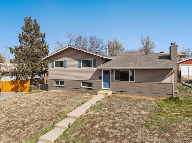 split level home featuring a chimney, brick siding, fence, and a front lawn
